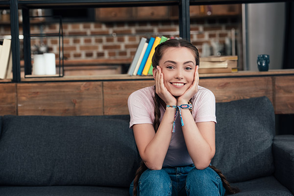 Smiling teenage girl sitting on couch with hands on cheeks